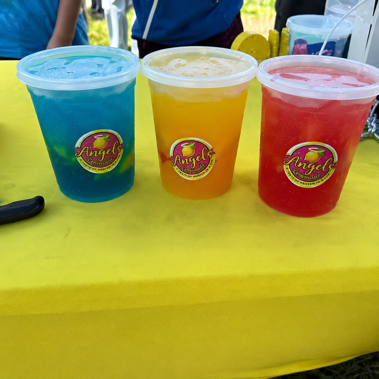 Three colorful handcrafted Angels Lemonade drinks in strawberry, mango, blue raspberry, and other fresh fruit flavors